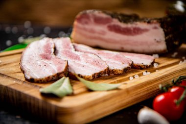 Pieces of homemade pork fat with green onions and cherry tomatoes. Against a dark background. High quality photo