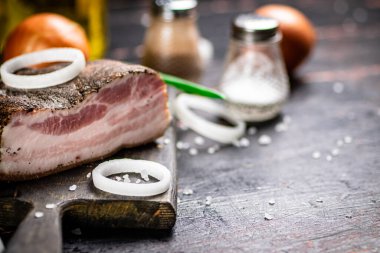 A piece of pork ladr with onion rings on a cutting board. Against a dark background. High quality photo