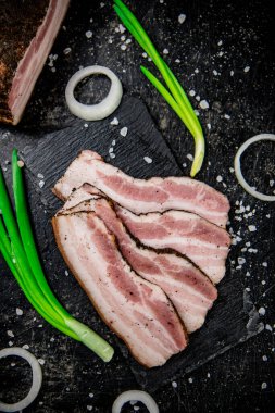 Delicious lard on a stone board with onions and spices. On a black background. High quality photo
