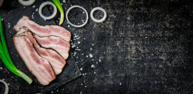 Delicious lard on a stone board with onions and spices. On a black background. High quality photo