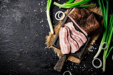 Pieces of lard on a cutting board with green onions. On a black background. High quality photo