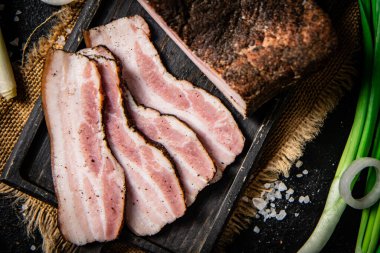 Pieces of lard on a cutting board with green onions. On a black background. High quality photo