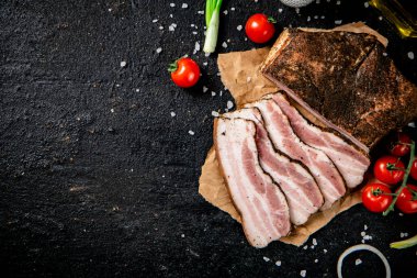 Pieces of lard on paper with onions and tomatoes. On a black background. High quality photo