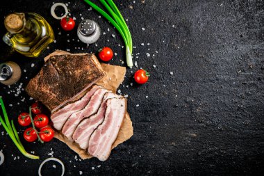 Pieces of lard on paper with onions and tomatoes. On a black background. High quality photo