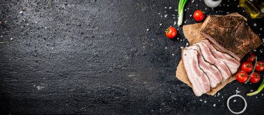 Pieces of lard on paper with onions and tomatoes. On a black background. High quality photo