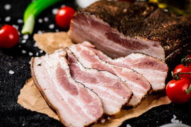 Pieces of lard on paper with onions and tomatoes. On a black background. High quality photo