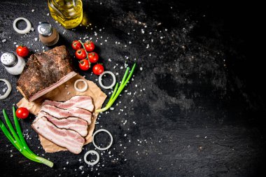 Pieces of lard on paper with onions and tomatoes. On a black background. High quality photo
