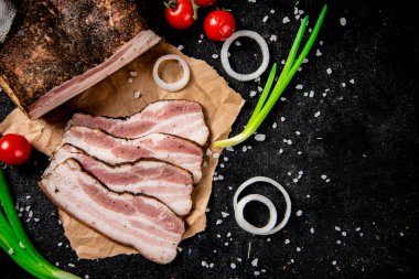 Pieces of lard on paper with onions and tomatoes. On a black background. High quality photo