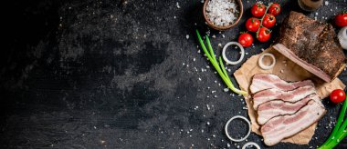 Pieces of lard on paper with onions and tomatoes. On a black background. High quality photo