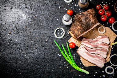 Pieces of lard on paper with onions and tomatoes. On a black background. High quality photo