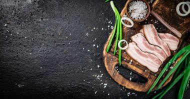 Chopped lard on a cutting board with green onions and spices. On a black background. High quality photo
