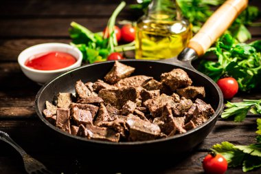 A frying pan with cooked liver on the table. On a wooden background. High quality photo