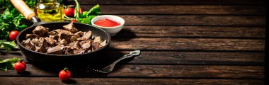 A frying pan with cooked liver on the table. On a wooden background. High quality photo