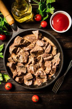 A frying pan with cooked liver on the table. On a wooden background. High quality photo