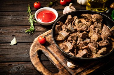 Fried liver in a frying pan on a cutting board with tomato sauce. On a wooden background. High quality photo
