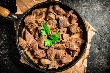 Liver in a frying pan on paper with a sprig of parsley. On a black background. High quality photo