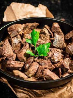 Liver in a frying pan on paper with a sprig of parsley. On a black background. High quality photo