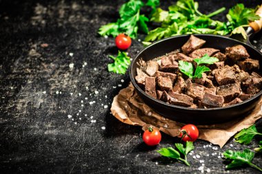 Liver cooked in a frying pan with cherry tomatoes and herbs. On a black background. High quality photo