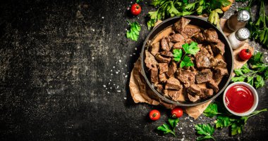 Liver cooked in a frying pan with cherry tomatoes and herbs. On a black background. High quality photo