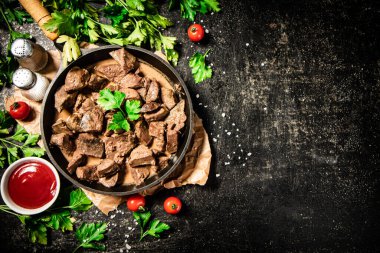 Liver cooked in a frying pan with cherry tomatoes and herbs. On a black background. High quality photo