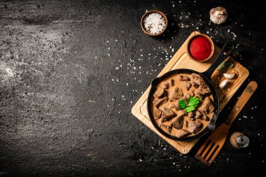 Delicious fried liver in a frying pan with tomato sauce. On a black background. High quality photo