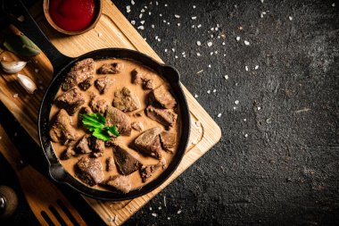 Delicious fried liver in a frying pan with tomato sauce. On a black background. High quality photo