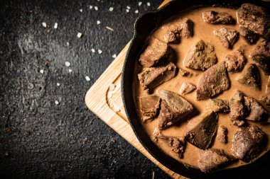 Liver cooked in a frying pan. On a black background. High quality photo