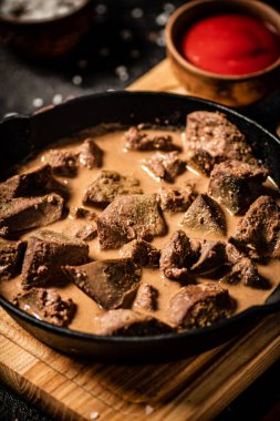 Delicious fried liver in a frying pan with tomato sauce. On a black background. High quality photo