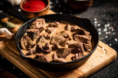 Delicious fried liver in a frying pan with tomato sauce. On a black background. High quality photo