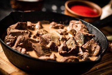 Delicious fried liver in a frying pan with tomato sauce. On a black background. High quality photo