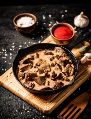 Delicious fried liver in a frying pan with tomato sauce. On a black background. High quality photo