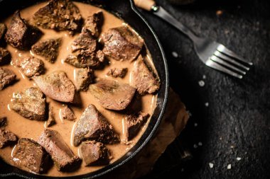 Liver cooked in a frying pan. On a black background. High quality photo