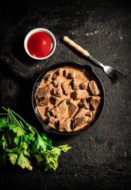 Delicious fried liver in a frying pan with tomato sauce and parsley. On a black background. High quality photo