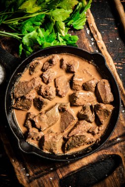 Liver in a frying pan on a cutting board with parsley and spices. Against a dark background. High quality photo