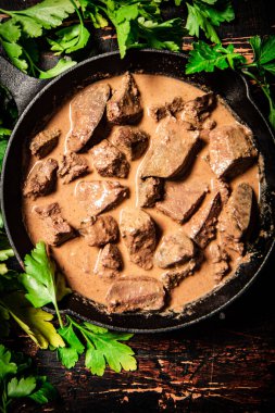 Cooked liver in a frying pan with parsley. Against a dark background. High quality photo