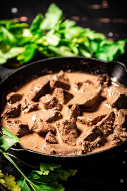 Cooked liver in a frying pan with parsley. Against a dark background. High quality photo