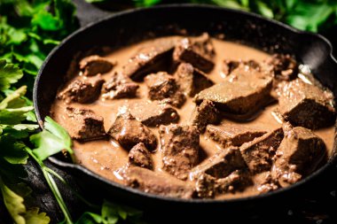 Cooked liver in a frying pan with parsley. Against a dark background. High quality photo