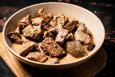 Fried liver in a bowl on a cutting board. Against a dark background. High quality photo