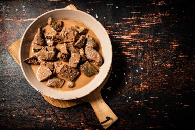 Fried liver in a bowl on a cutting board. Against a dark background. High quality photo