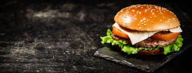 A burger on a stone board on a table. On a black background. High quality photo