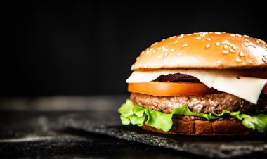 A burger on a stone board on a table. On a black background. High quality photo