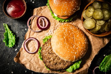Delicious burger with lettuce leaves and onion rings. On a black background. High quality photo