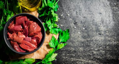 Sliced raw liver in a bowl with parsley. On a black background. High quality photo