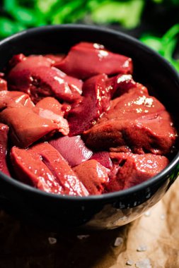 Sliced raw liver in a bowl with parsley. On a black background. High quality photo