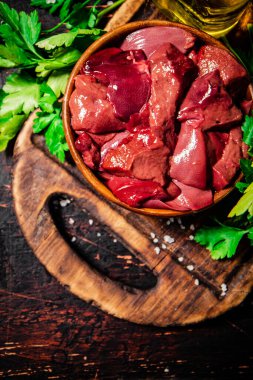 Pieces of raw liver in a bowl on a parsley cutting board. Against a dark background. High quality photo