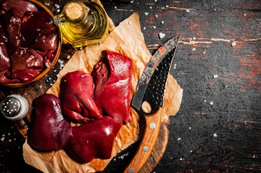 Pieces of raw liver on a cutting board with oil and spices. Against a dark background. High quality photo