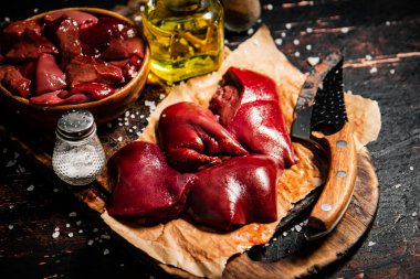 Pieces of raw liver on a cutting board with oil and spices. Against a dark background. High quality photo