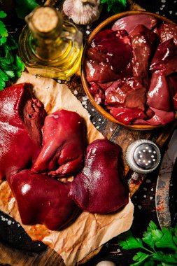 Pieces of raw liver with spices, oil and herbs. Against a dark background. High quality photo