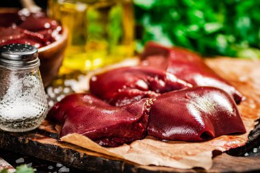 Pieces of raw liver with spices, oil and herbs. Against a dark background. High quality photo