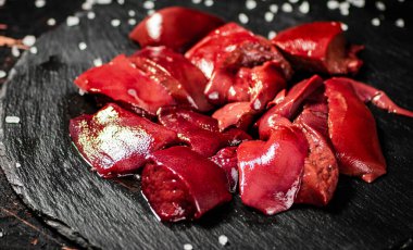 Pieces of raw liver on a stone tray with salt. Against a dark background. High quality photo